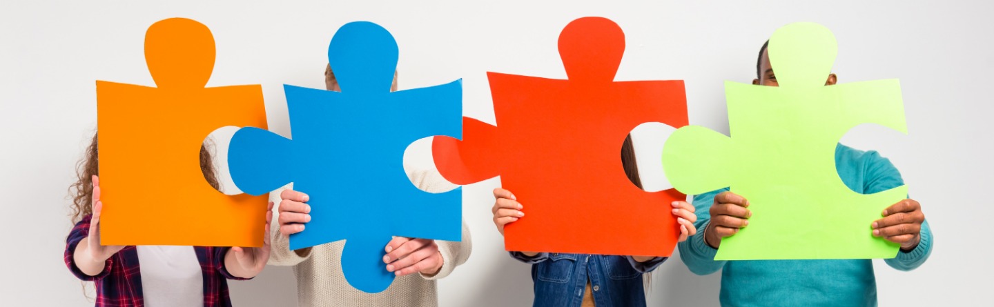 Header: Mehrere Personen halten große Puzzlestücke, als Symbol für den Autismus, vor ihr Gesicht.