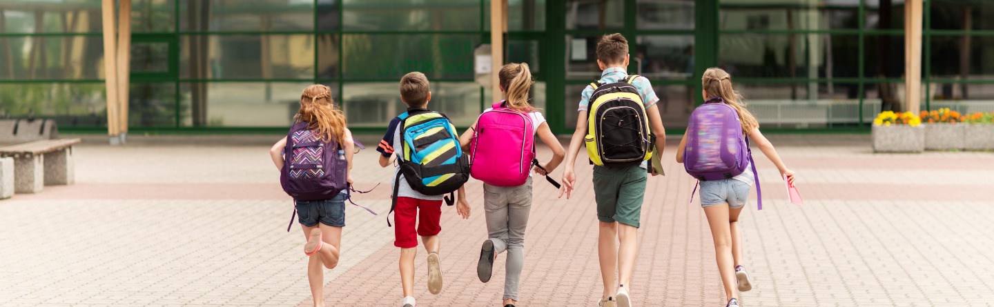 Header: Fünf junge Schulkinder laufen auf ihr Schulgebäude zu. 