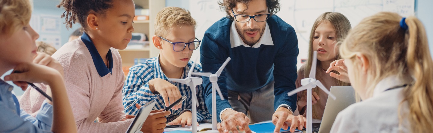 Header: Einige Schulkinder arbeiten gemeinsam mit ihrem Lehrer an einem Projekt. 