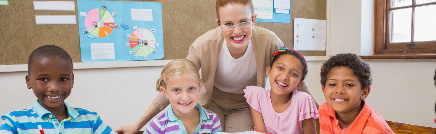 Header: Vier Kinder lächeln gemeinsam mit ihrer Lehrerin in die Kamera. 