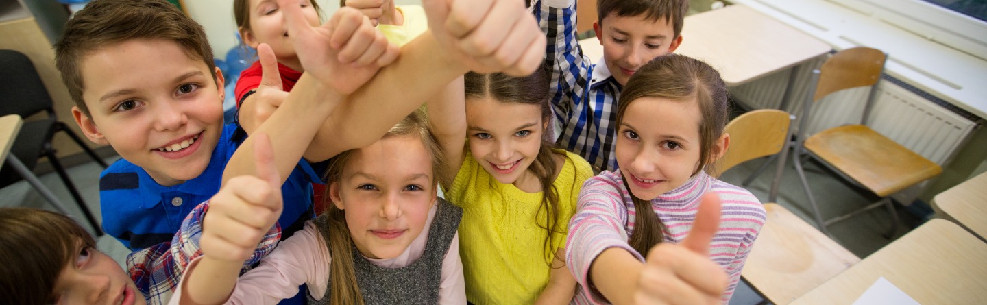 Kinder halten in einem Klassenzimmer den Daumen nach oben und lachen