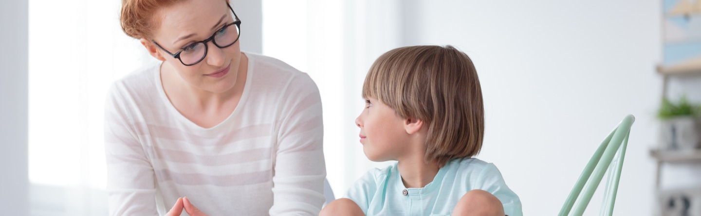 Header: Ein kleiner Junge sitzt im Schneidersitz neben einer Frau und redet mit ihr. 
