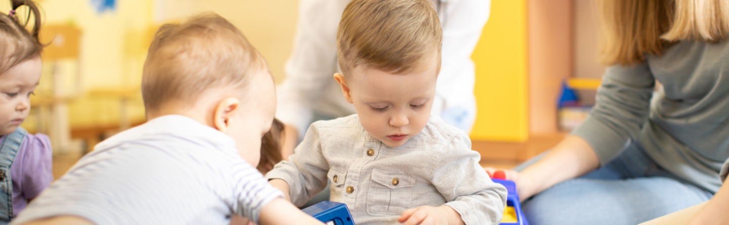 Header: Drei Kleinkinder spielen gemeinsam mit ihren Betreuerinnen 