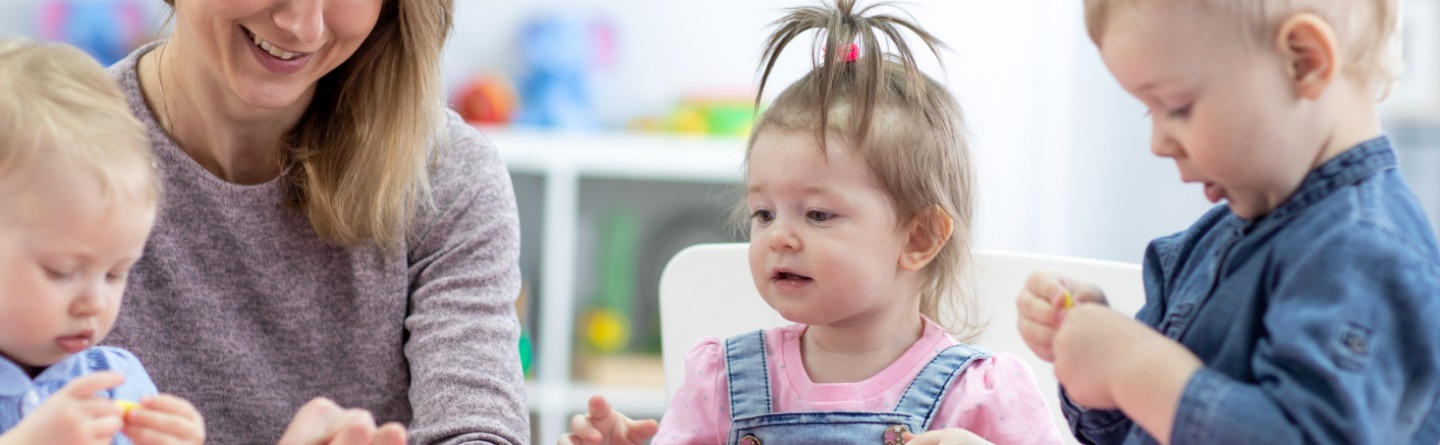 Header: Drei Kleinkinder spielen gemeinsam mit ihrer Betreuerin 