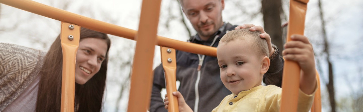 Header: Ein Kleinkind spielt gemeinsam mit seinen Eltern auf einem Spielplatz. 
