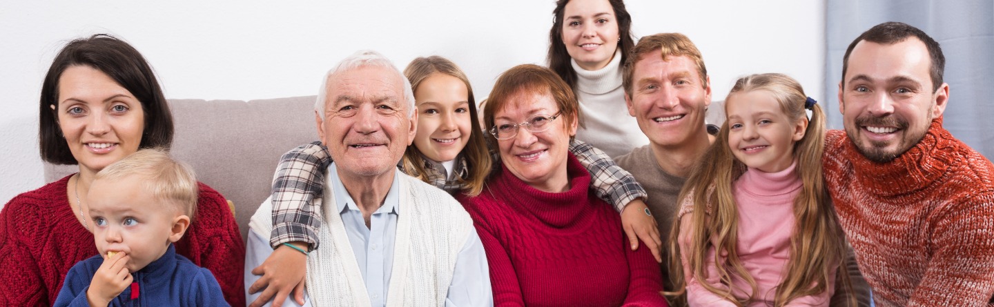 Header: Eine große Familie sitzt gemeinsam auf einem Sofa. Alle lächeln in die Kamera. 