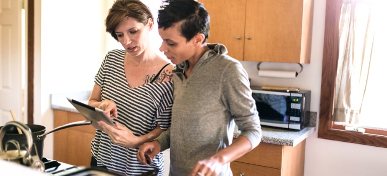 Header: Ein junger Mann steht mit seiner Betreuerin in seiner Küche. Sie unterstützt ihn beim Kochen. 