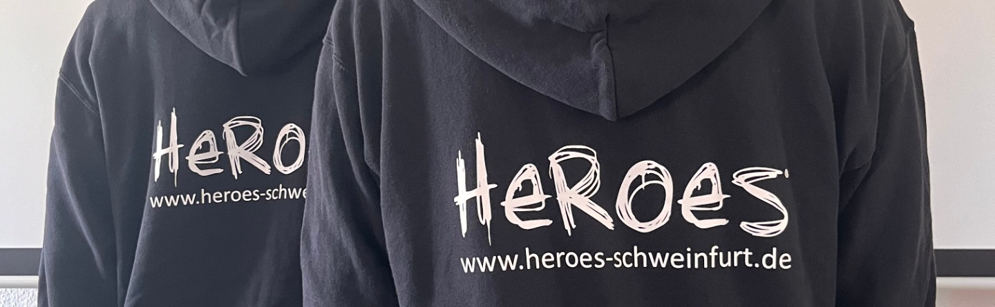Header: zwei Junger Männer sind von hinten zu sehen. Beide tragen einen schwarzen Pulli auf dem groß HEROES steht. 