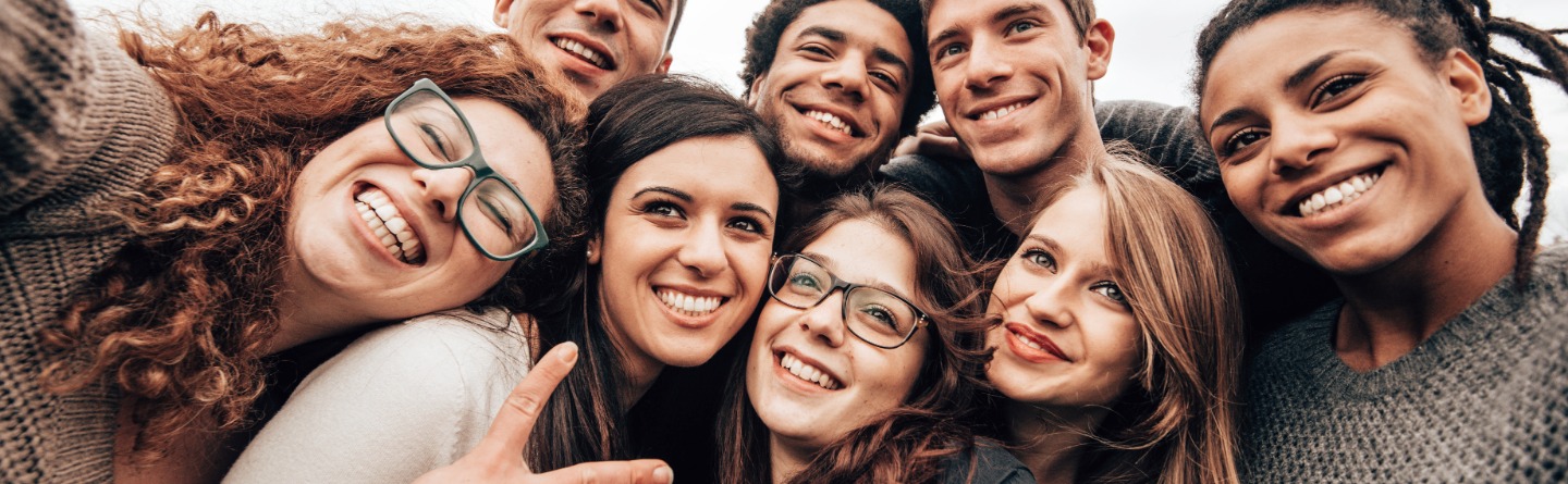 Header: Einige junge Erwachsene nehmen zusammen ein Selfie auf. Alle lächeln und sind fröhlich. 