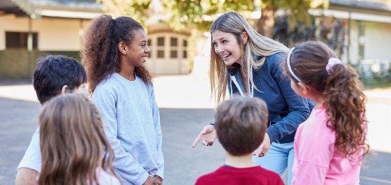 Jugendsozialarbeit an Schulen Kachel: Eine Frau spricht mit einer Gruppe von Schülerinnen und Schülern.