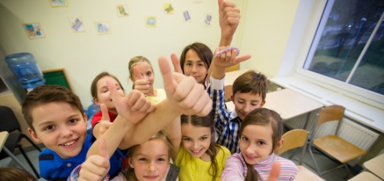 Kinder halten in einem Klassenzimmer den Daumen nach oben und lachen