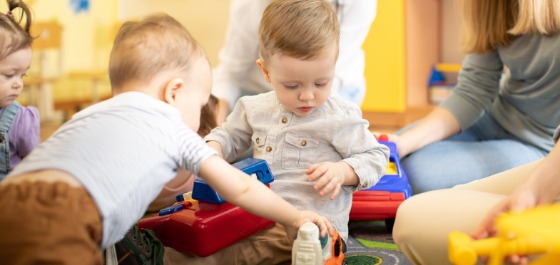 Kachel: Drei Kleinkinder spielen gemeinsam mit ihren Betreuerinnen 