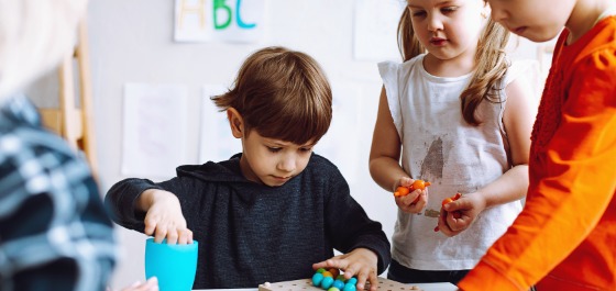 Kachel: Ein paar Kinder spielen im Kindergarten mit Holzkugeln 