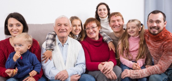 Kachel: Eine große Familie sitzt gemeinsam auf einem Sofa. Alle lächeln in die Kamera. 
