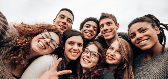 Kachel: Einige junge Erwachsene nehmen zusammen ein Selfie auf. Alle lächeln und sind fröhlich. 