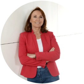 Frau mit rotem Blazer und blauer Jeans lehnt an Wand - Ingrid Schmidt