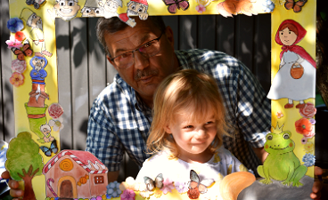 Märchenhafter Geburtstag: “Kinderwiese” feiert fünfjähriges Jubiläum News- Foto: Ein Mann und ein Mädchen schauen gemeinsam durch einen bunt verzierten, kindlich gestalteten Bilderrahmen mit Märchenmotiven