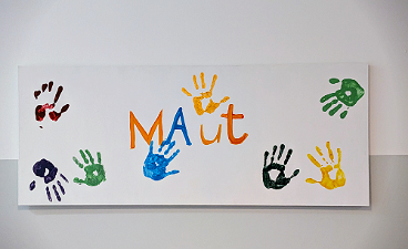 News- Foto: Eine weiße Landwand mit bunten Handabdrücken und dem Begriff "MAut" in der Mitte
