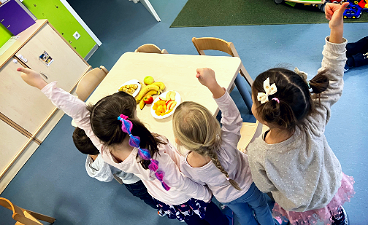 News- Foto: Vier Kinder stehen um einen Tisch voller Obst und strecken ihre Daumen nach oben