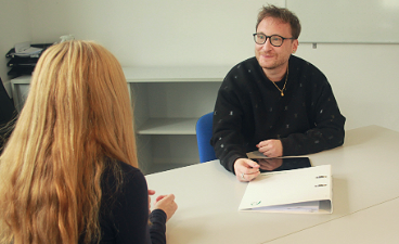 News- Foto: Ein Mann sitzt einem Mädchen an einem Tisch gegenüber