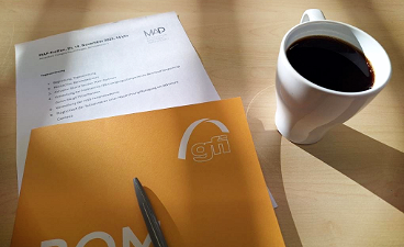 News- Foto: Eine gfi- Mappe inkl. Kugelschreiber liegt auf einem Schreibtisch, daneben eine gefüllte Kaffeetasse