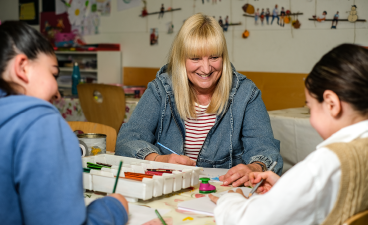 Gemeinsam kreativ: Malen im KoGa mit Betreuerin und Schülerinnen. KoGa-News-Foto: Kreatives Miteinander – Eine Betreuerin im kreativen Austausch mit Schülerinnen.