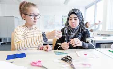 News- Foto: Zwei Schülerinnen sitzen bastelnd an einem Tisch