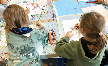 Zwei Kinder, die von hinten zu sehen sind, sitzen an einem Tisch und malen