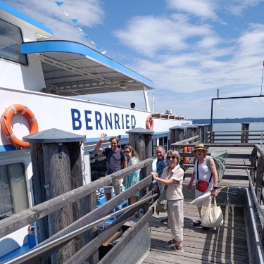 Fünf Personen stehen auf dem Holzsteg und besteigen das Schiff  MS Bernried der  Schifffahrt Starnberger See