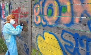 Eine Schülerin sprüht mit eine Dose ein Graffiti an einen hölzernen Zaun