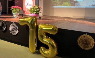 Eine aus zwei Luftballons bestehende goldene 75 steht vor einer festlich geschmückten Bühne.